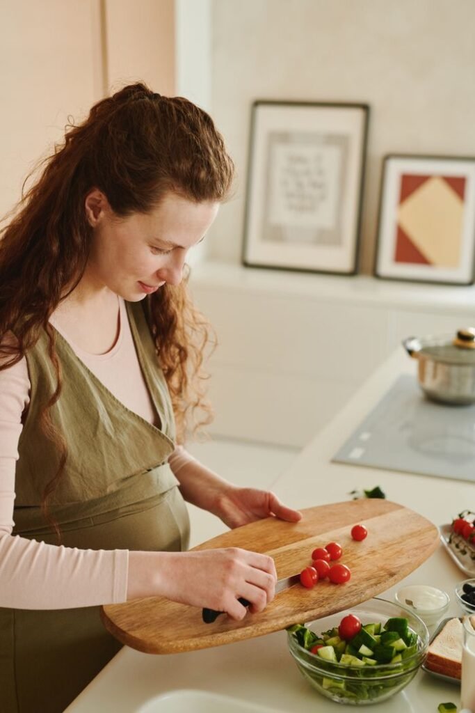 Expectant mother chopping vegetables for a fresh salad in her kitchen.